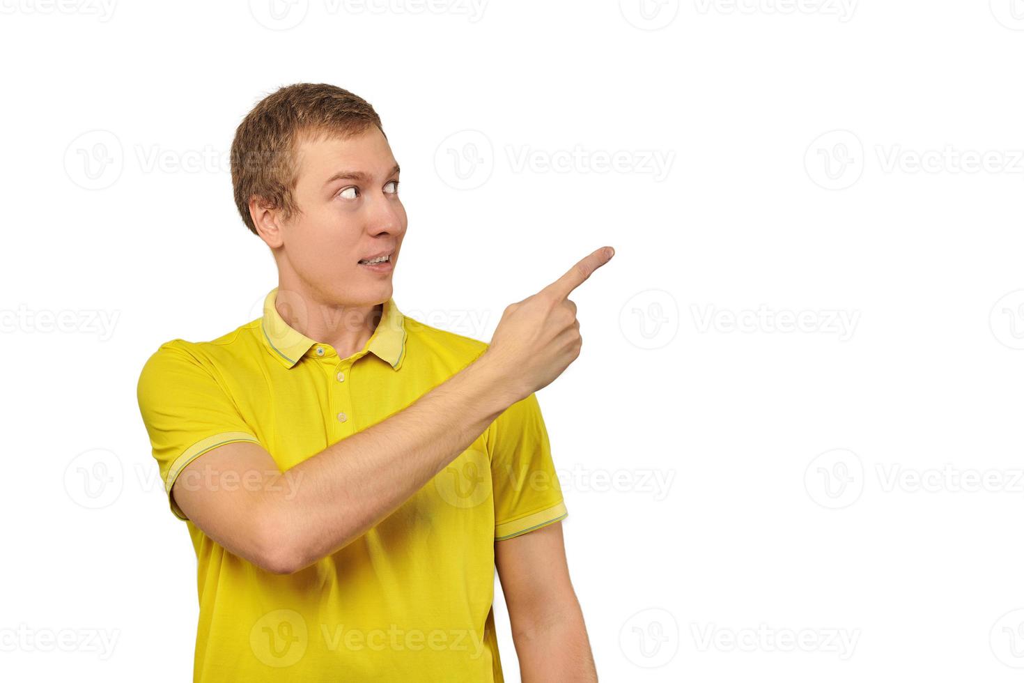 Guy surpris avec drôle de visage en t-shirt jaune vif pointant le doigt vers la droite, fond blanc photo