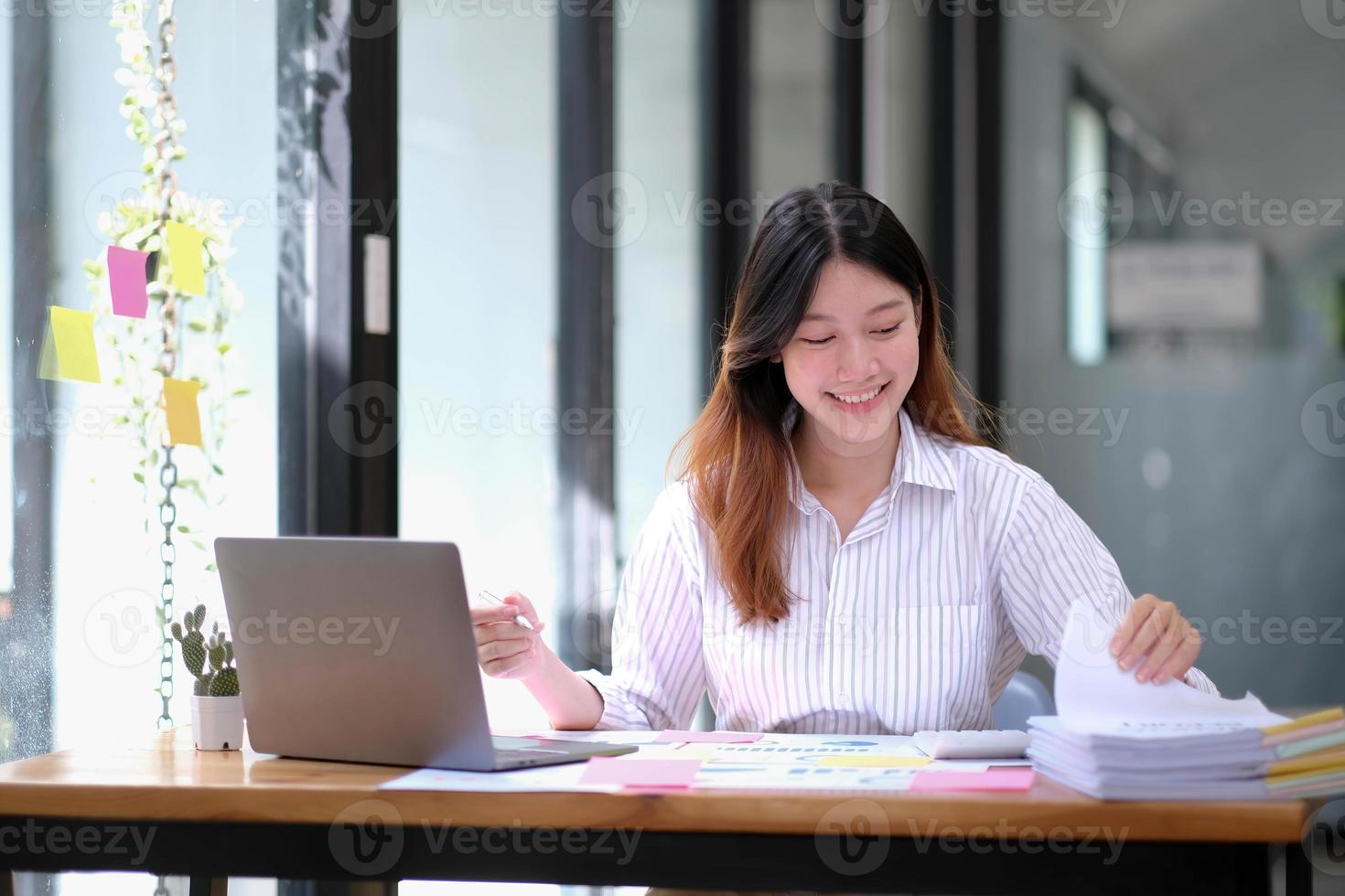 souriante jeune femme d'affaires asiatique travaillant avec une calculatrice, un document commercial et un ordinateur portable, un inspecteur financier et une secrétaire faisant un rapport, un document de vérification du service des recettes internes. photo