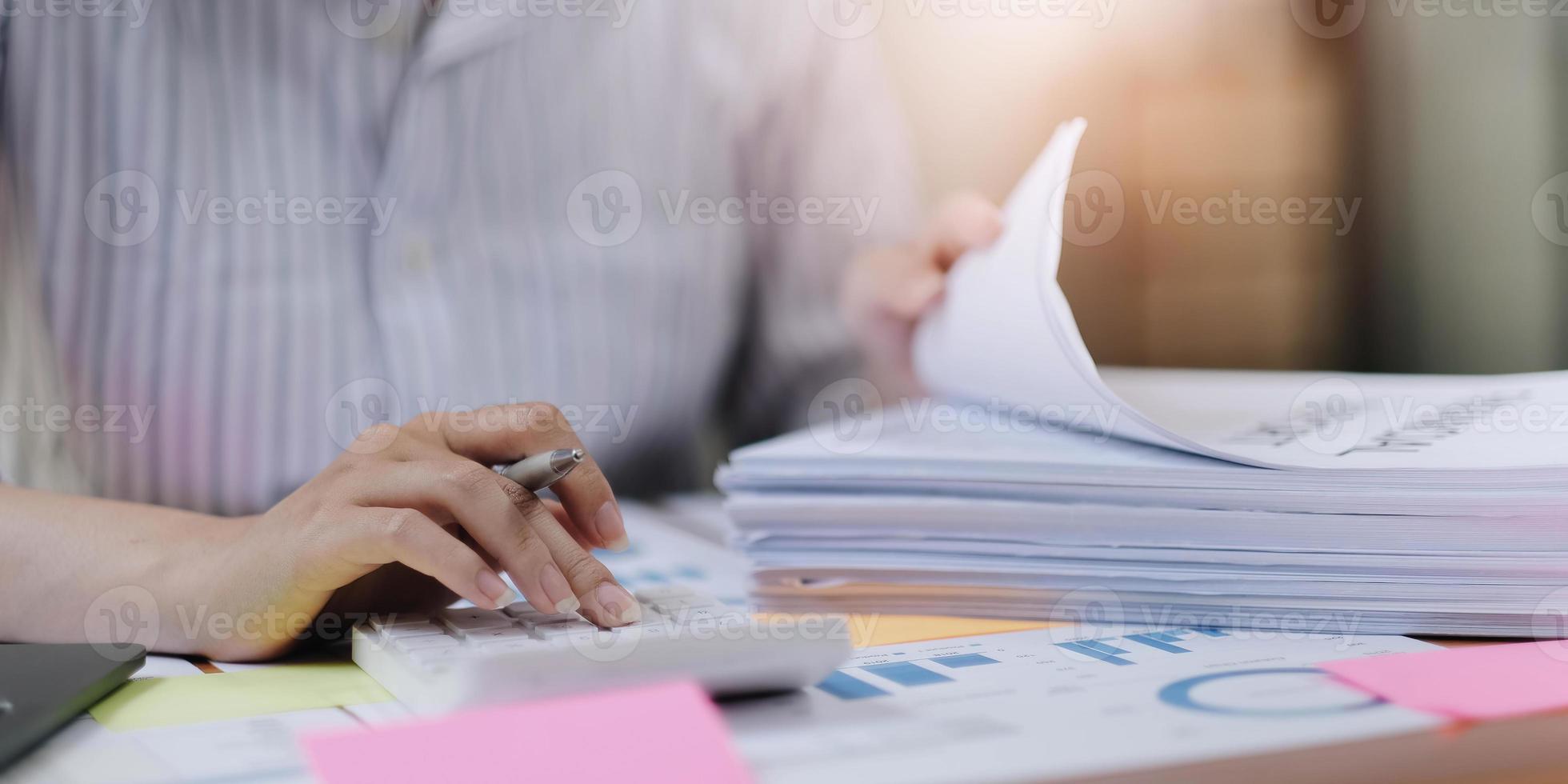 Gros plan de femme d'affaires ou comptable main tenant un stylo travaillant sur la calculatrice pour calculer les données commerciales, document de comptabilité et ordinateur portable au bureau, concept d'entreprise photo