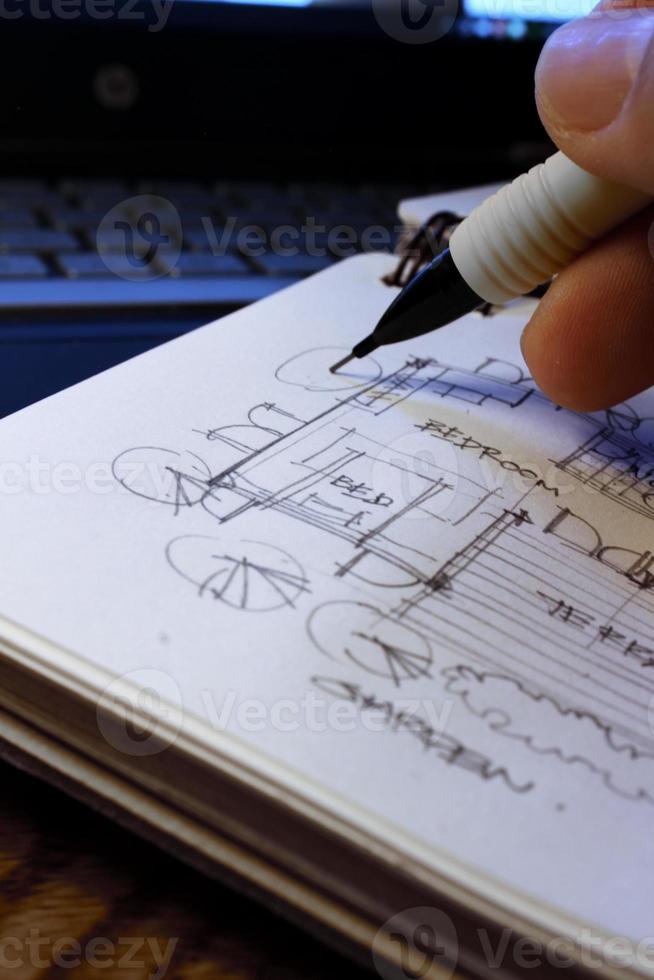 les mains de l'architecte dessinent des plans architecturaux avec des crayons sur un carnet de croquis sur un bureau avec un ordinateur portable. photo