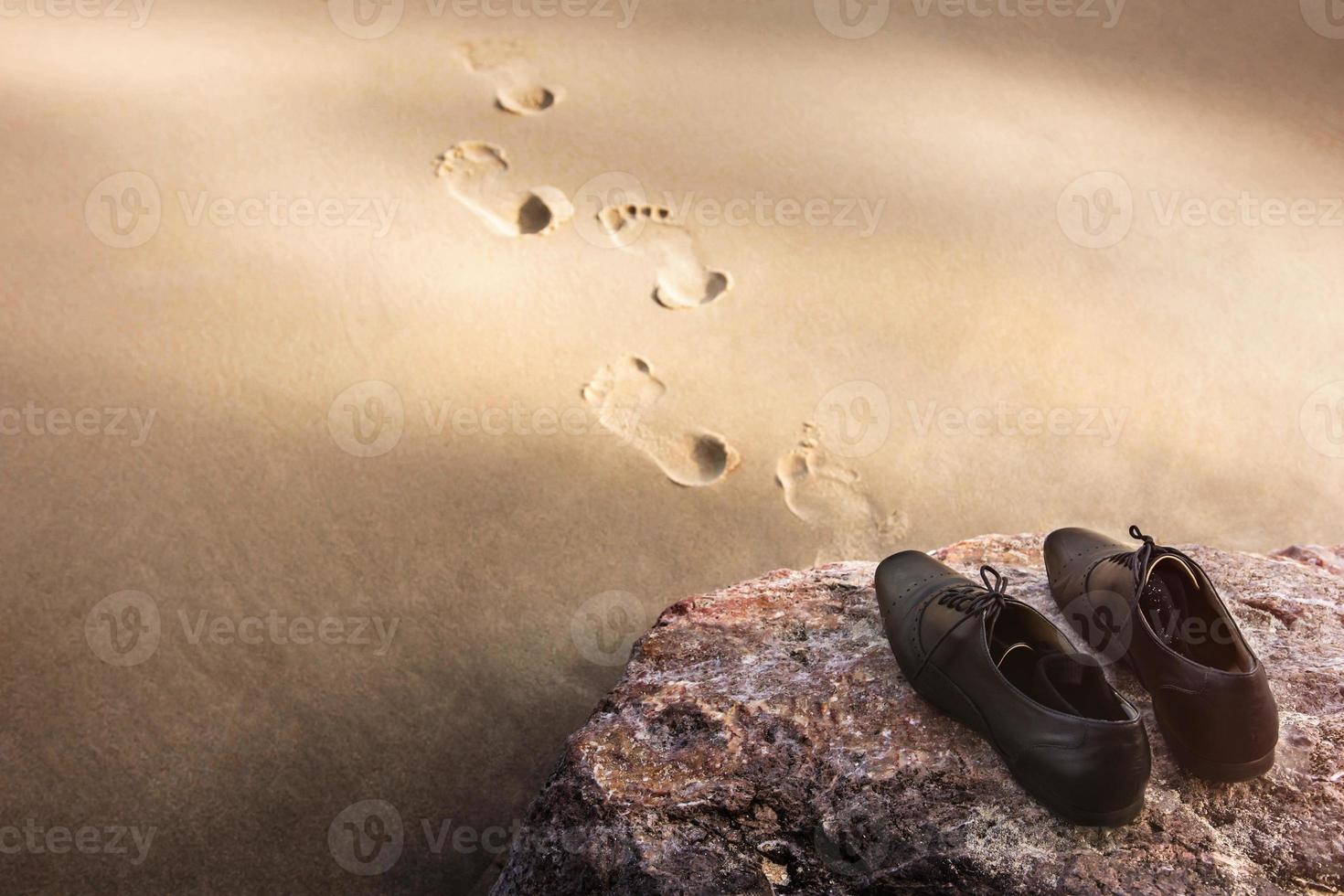 concept d'équilibre travail-vie personnelle, l'homme d'affaires enlève ses chaussures oxford de travail et les laisse sur le rocher de la plage pour se promener dans la mer par temps ensoleillé. empreinte sur le sable. vue de dessus photo