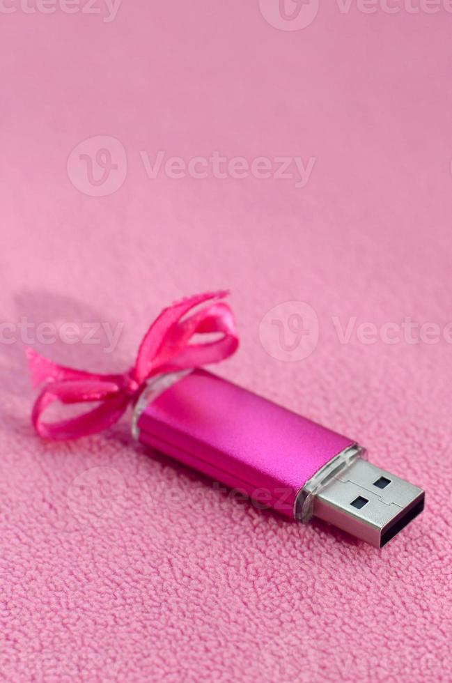 carte mémoire flash usb rose brillante avec un arc rose se trouve sur une couverture en tissu polaire rose clair doux et poilu. conception de cadeau féminin classique pour une carte mémoire photo