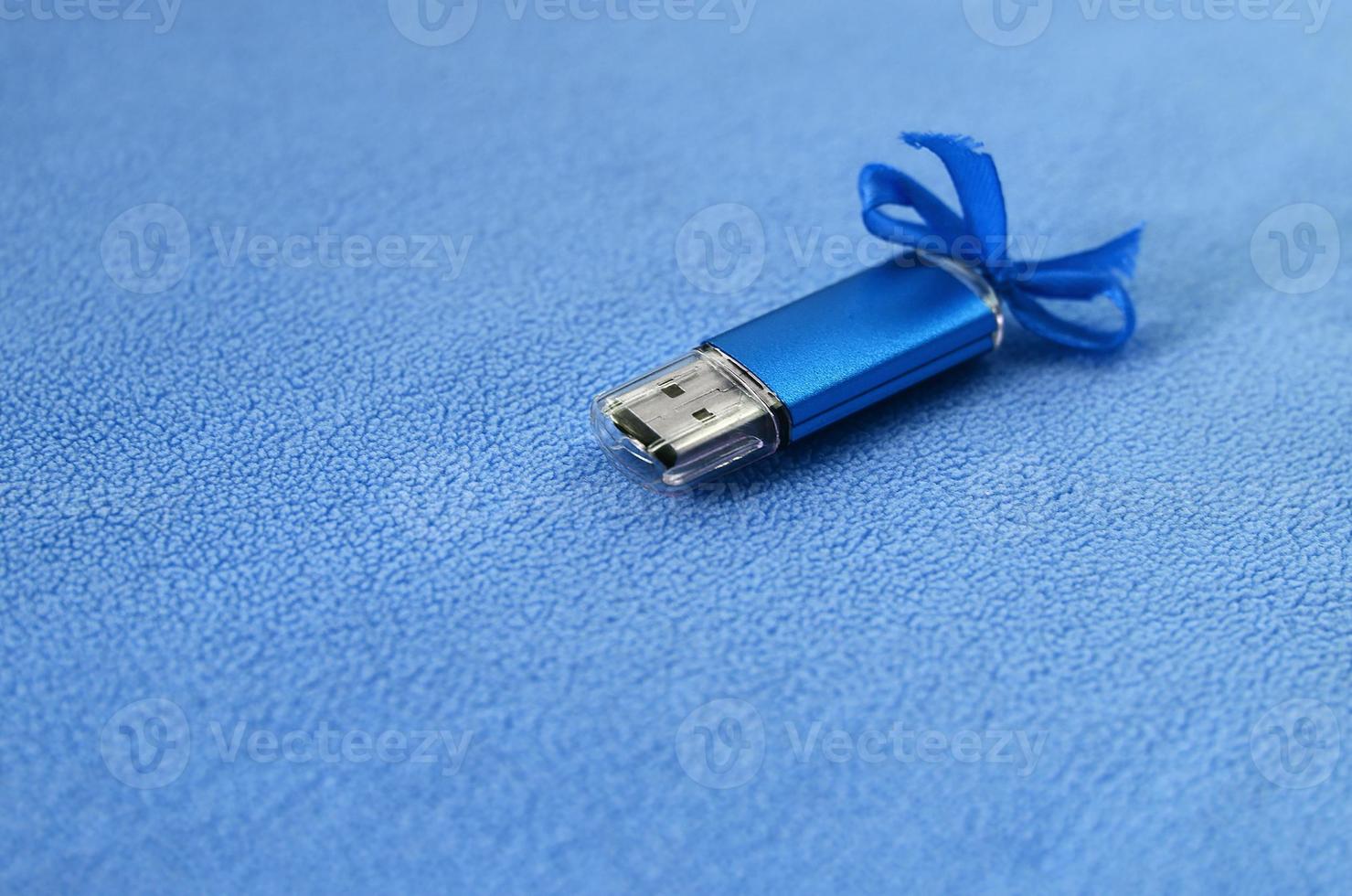 carte mémoire flash usb bleu brillant avec un arc bleu se trouve sur une couverture de tissu polaire bleu clair doux et poilu. conception de cadeau féminin classique pour une carte mémoire photo