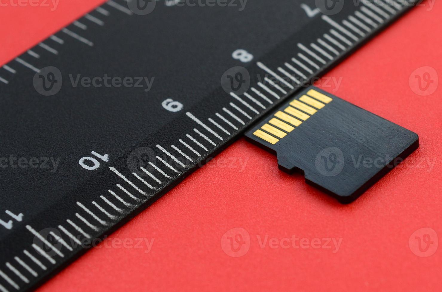 une petite carte mémoire micro sd se trouve sur un fond rouge à côté d'une règle noire. un magasin de données et d'informations petit et compact photo