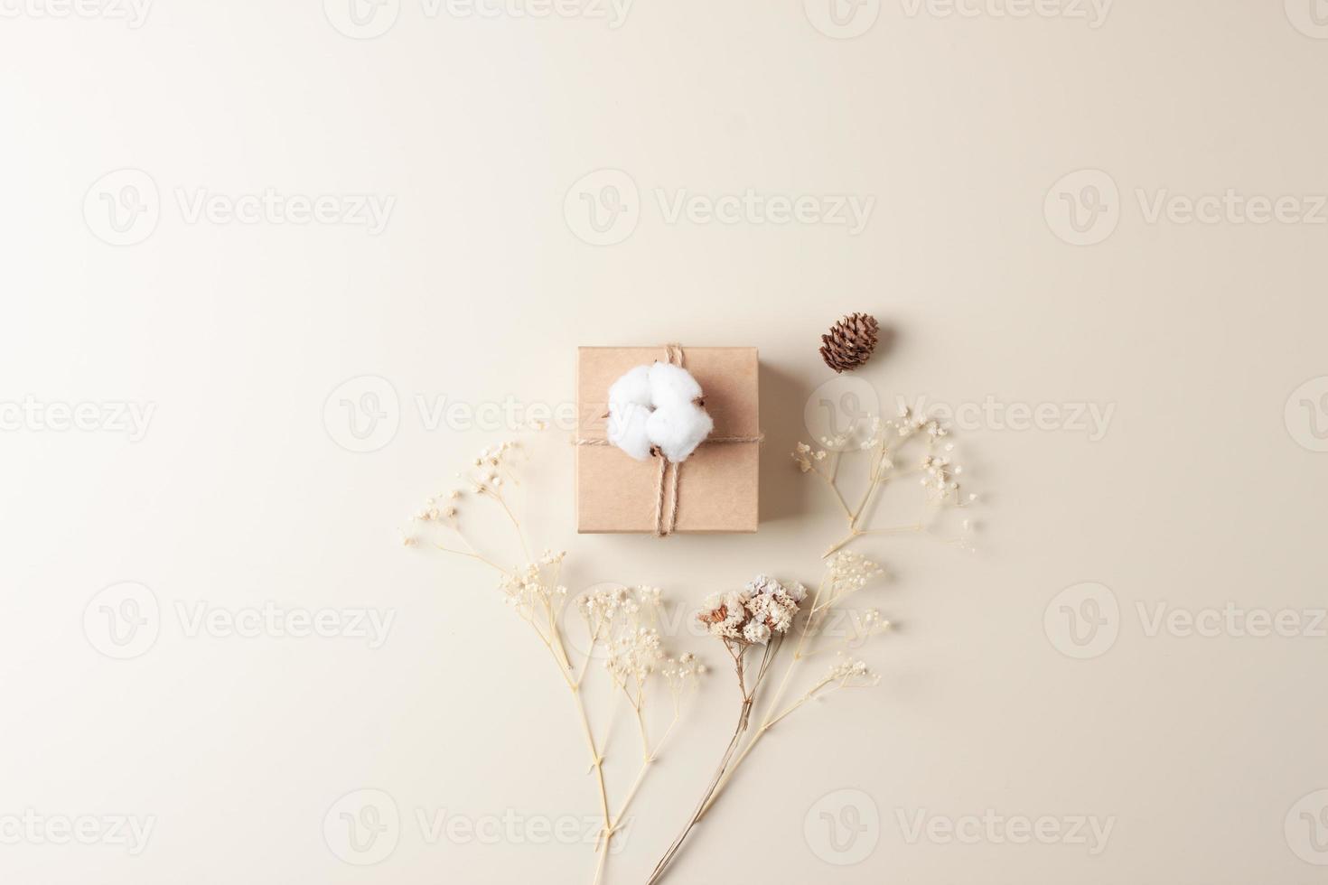 composition minimale de noël avec cadeau d'emballage en papier kraft et fleurs sur fond beige. mise à plat, espace de copie photo