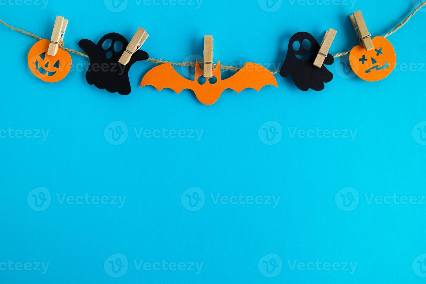 décorations de vacances pour halloween. fantômes en papier noir et citrouilles en papier orange et chauve-souris suspendus à une corde sur fond bleu avec espace de copie. photo