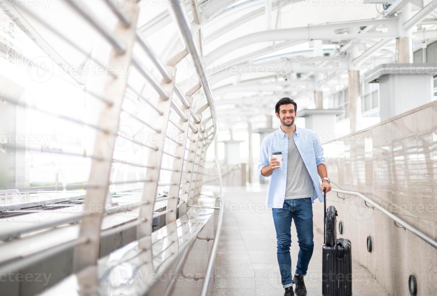 l'homme tenant une tasse de café et tirant les bagages pendant qu'il attend son ami à l'aéroport. photo