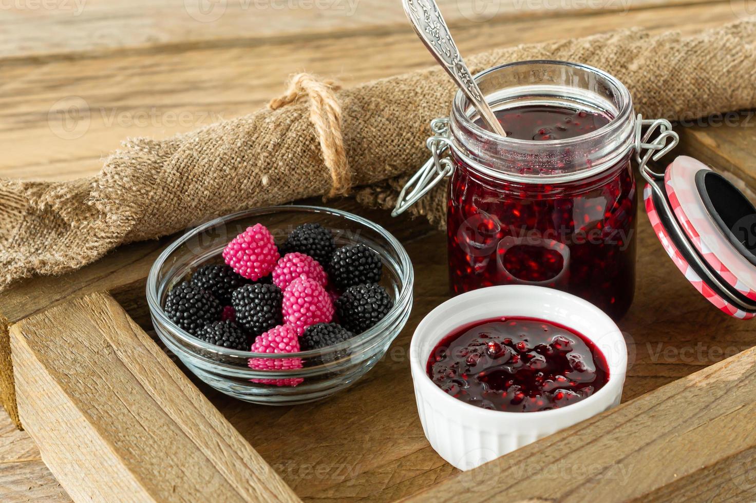 mâcher des bonbons à la gelée de marmelade au goût de baies sur une table en bois avec de la confiture dans un bocal en verre. photo