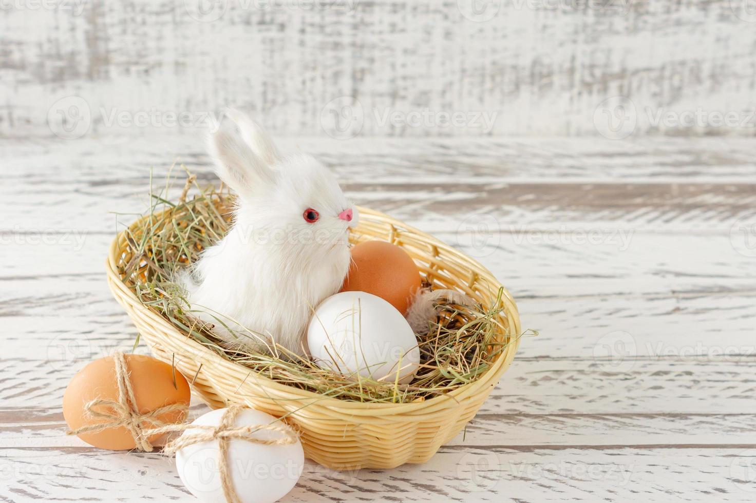 composition festive de pâques avec petit lapin assis dans un panier avec oeuf de pâques. style rustique, concept écologique et fermier photo