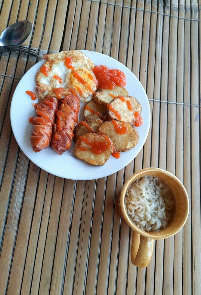 le menu du petit-déjeuner de ce matin est accompagné de saucisses, de pommes de terre et d'œufs, il y a aussi des nouilles dans un verre qui complètent la sauce photo