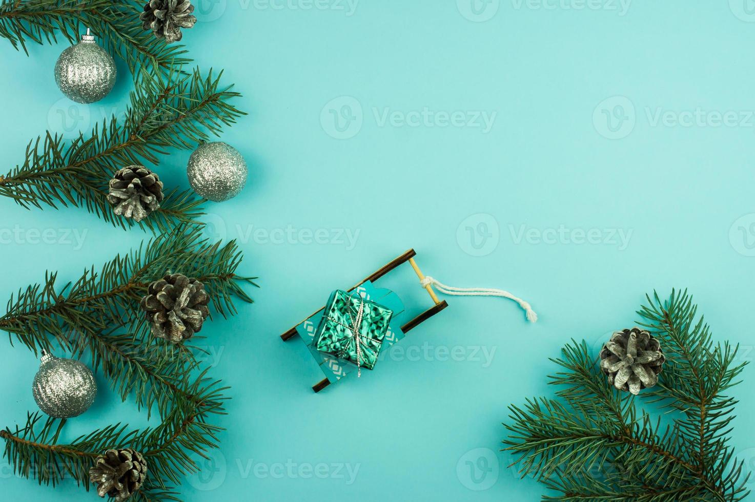 composition du nouvel an avec des branches décorées de boules et de cônes d'épinette argentée. traîneau décoratif avec un cadeau sur fond bleu. espace de copie. photo