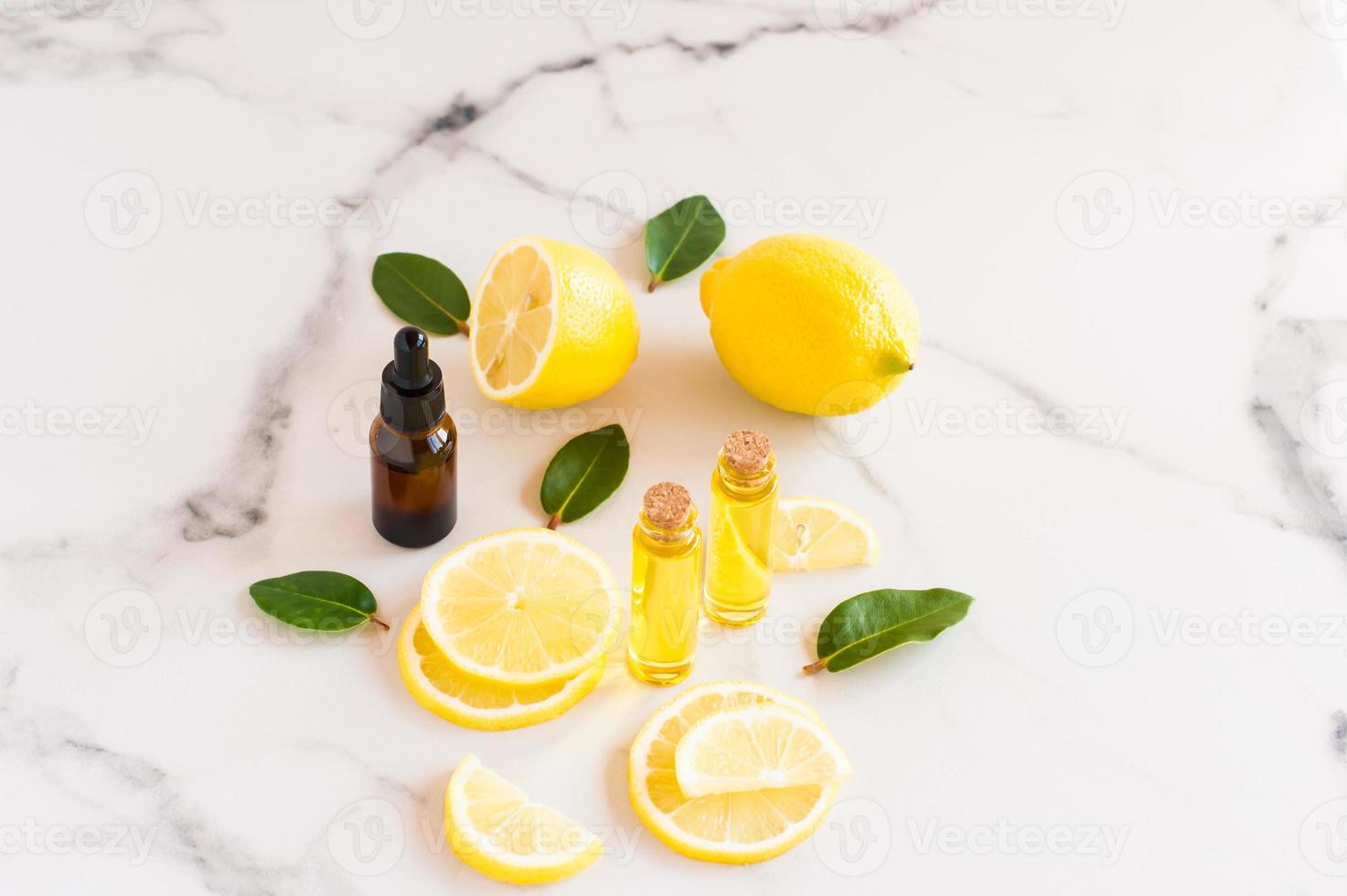 huile de citron cosmétique et huile essentielle d'agrumes sur une table en marbre. fruits de citron frais et feuilles de melisa. cosmétiques de la nature dans des bouteilles en verre. photo