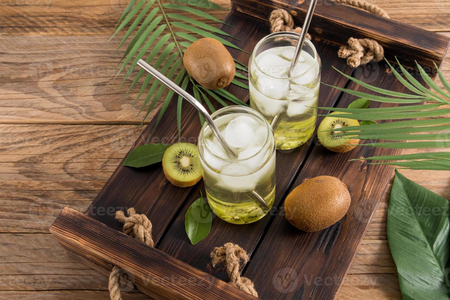 deux verres modernes sous forme de canette de bière avec une boisson douce et saine au kiwi et des morceaux de glace sur un plateau en bois. photo