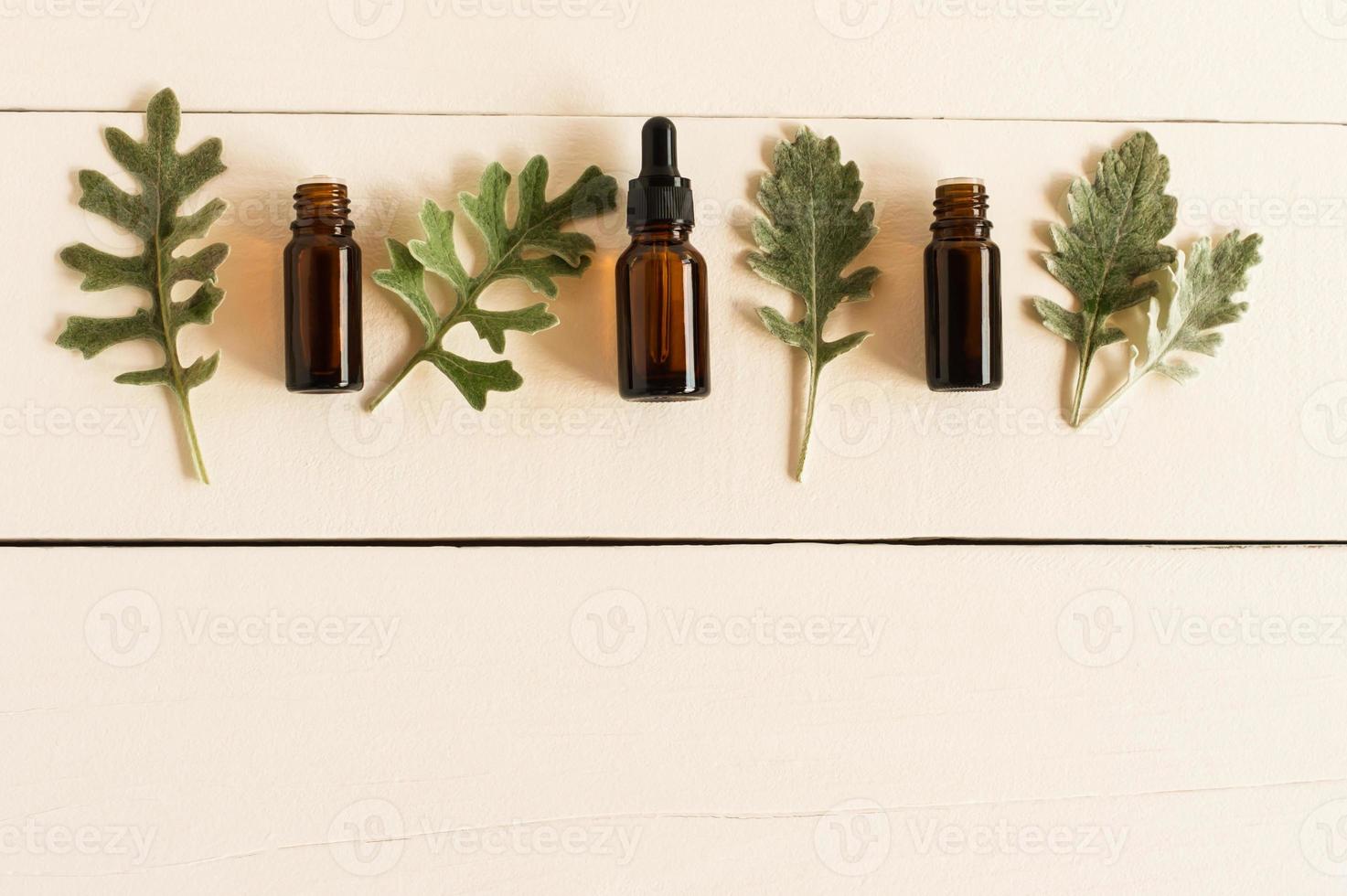 huile aromatique essentielle avec des ingrédients naturels sur le fond d'une table en bois blanche avec des feuilles grises de plantes. mise à plat. photo