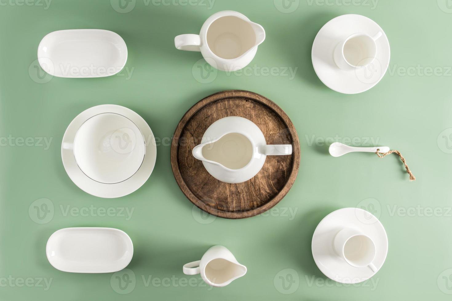 tasses en céramique et porcelaine blanches, soucoupes, pot à lait de différentes formes sur fond vert clair. vue de dessus. mise à plat. photo