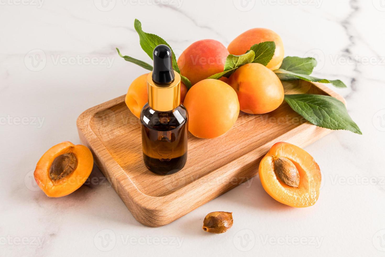 le parfait produit de soin de la peau du visage. huile de noyau d'abricot dans une bouteille cosmétique avec une pipette sur un plateau en bois et un fond en marbre. photo