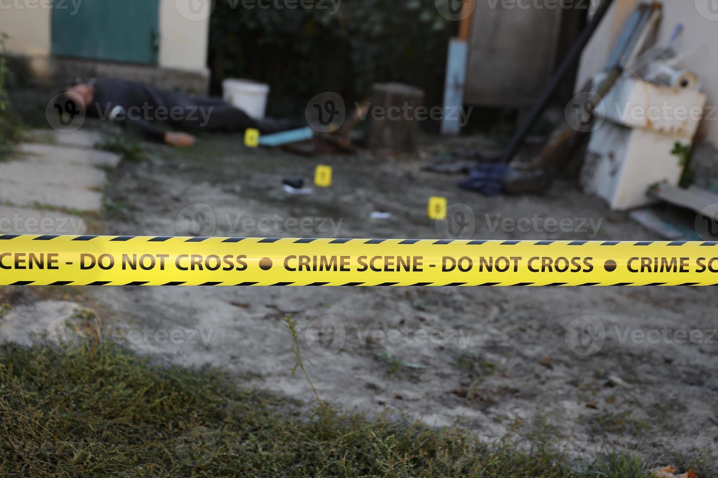 victime d'un crime violent dans une arrière-cour d'une maison d'habitation en soirée. corps d'homme mort sous la bande jaune de la ligne de police et marqueurs de preuve sur la scène du crime photo