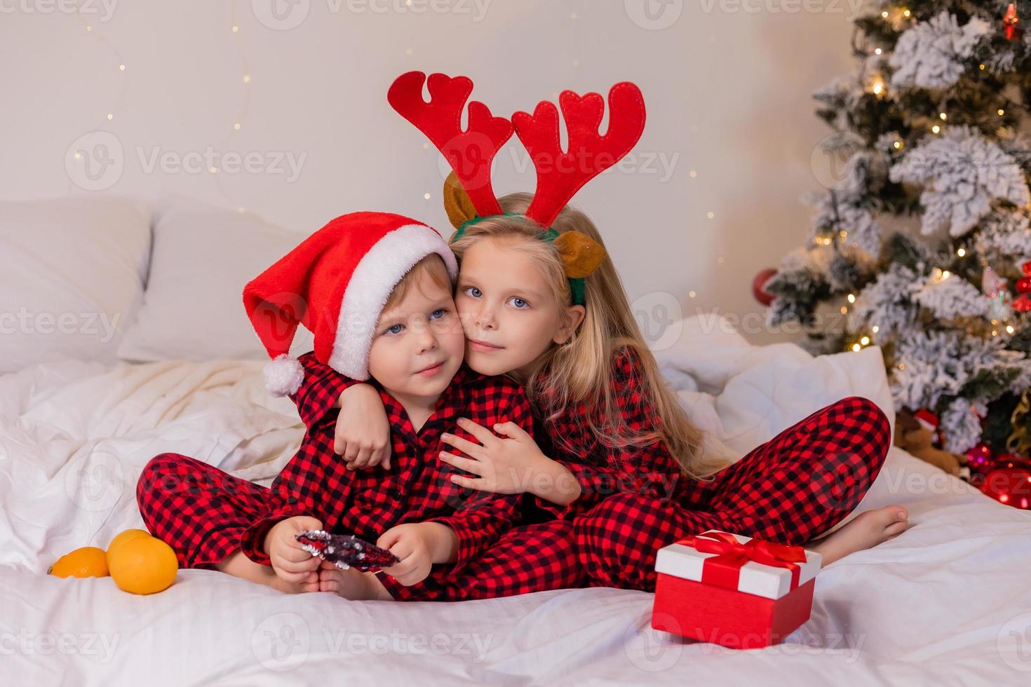 deux enfants à la maison en pyjama pour noël trient des cadeaux et se blottissent au lit sur fond d'arbre de noël photo