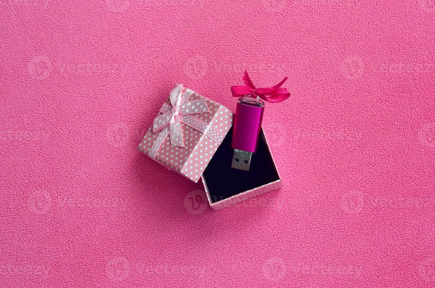 La carte mémoire flash USB rose brillante avec un nœud rose se trouve dans une petite boîte cadeau en rose avec un petit nœud sur une couverture en tissu polaire rose clair doux et poilu. conception de carte mémoire cadeau femme classique photo