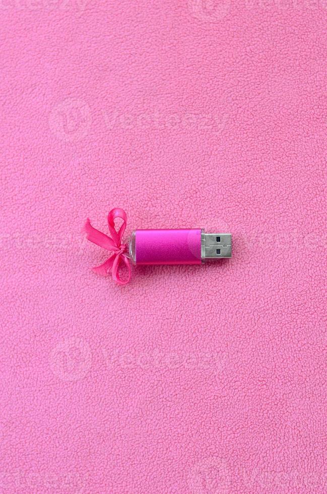 carte mémoire flash usb rose brillante avec un arc rose se trouve sur une couverture en tissu polaire rose clair doux et poilu. conception de cadeau féminin classique pour une carte mémoire photo