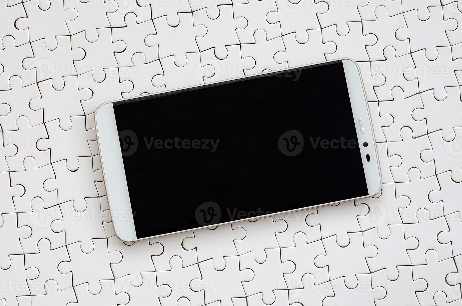 un grand smartphone moderne avec un écran tactile se trouve sur un puzzle blanc à l'état assemblé photo