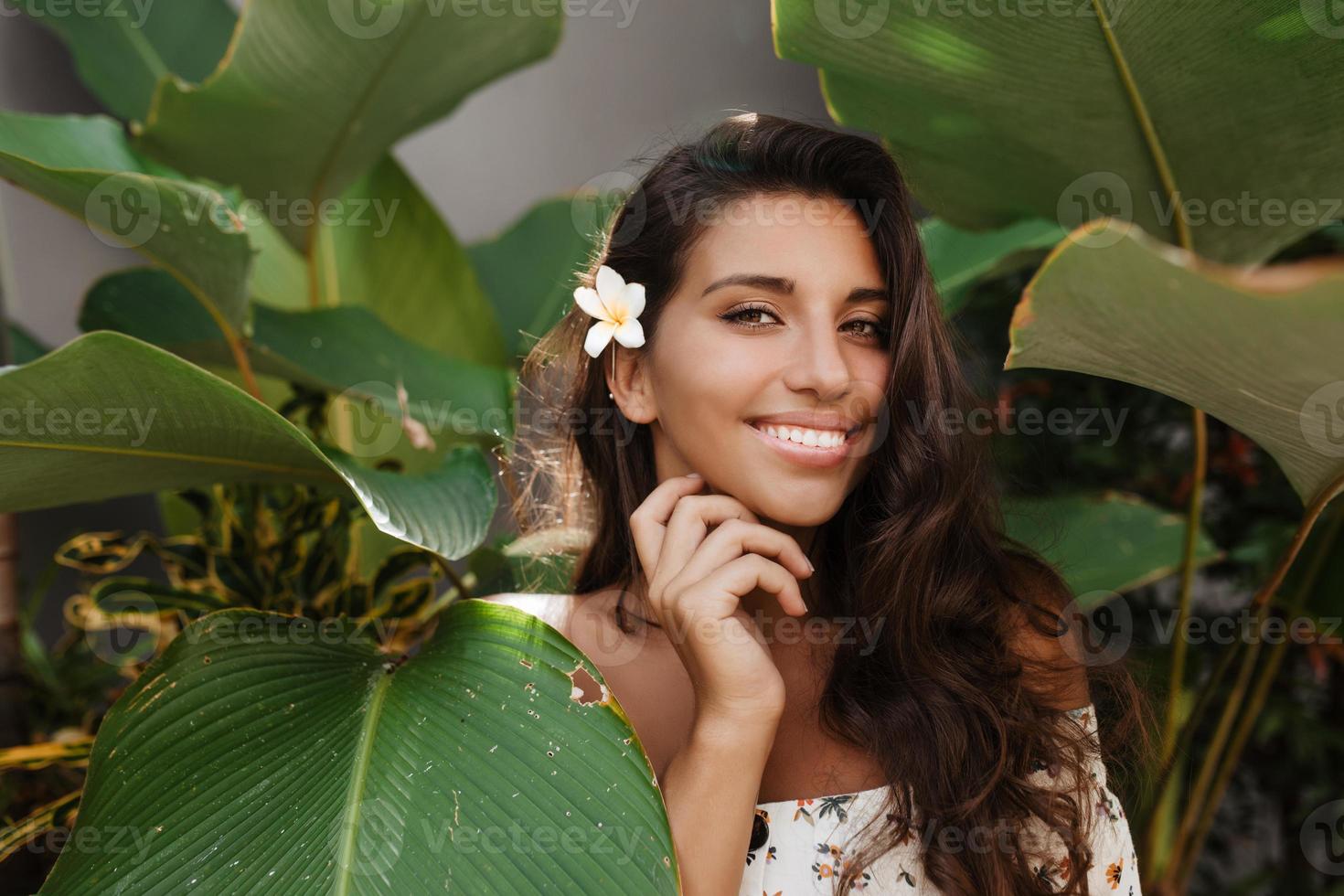 dame bronzée aux yeux verts en haut blanc et avec une petite fleur dans ses longs cheveux avec un charmant sourire photo
