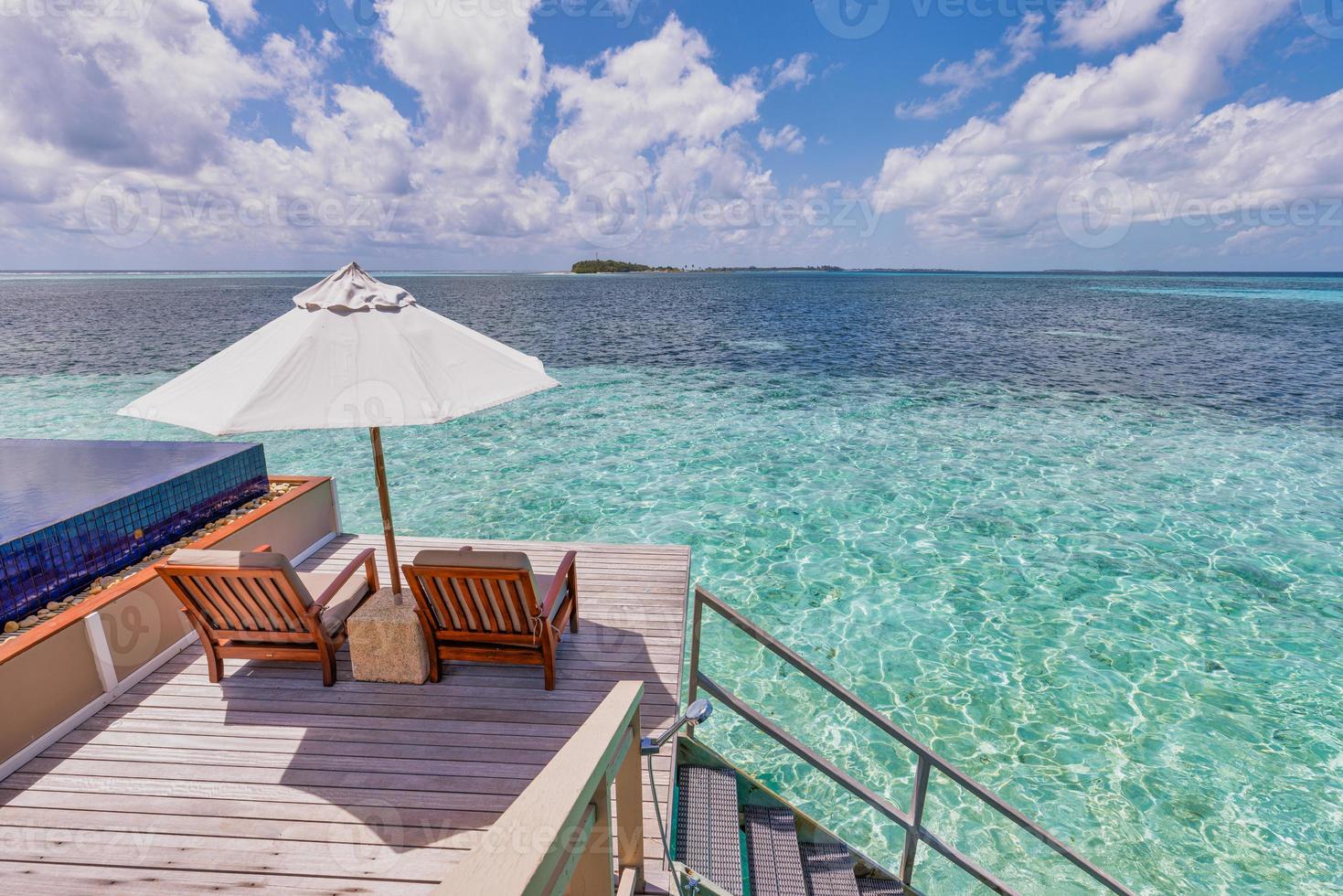 chaise longue avec parasols au complexe des maldives avec piscine à débordement et plage, vue sur le ciel de la mer. villa de luxe sur l'eau, lune de miel sur une île paradisiaque, destination de couple romantique. retraite de loisirs de détente d'été photo