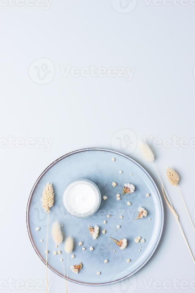 pot de crème cosmétique avec des fleurs sèches sur fond gris. mise à plat, espace de copie photo