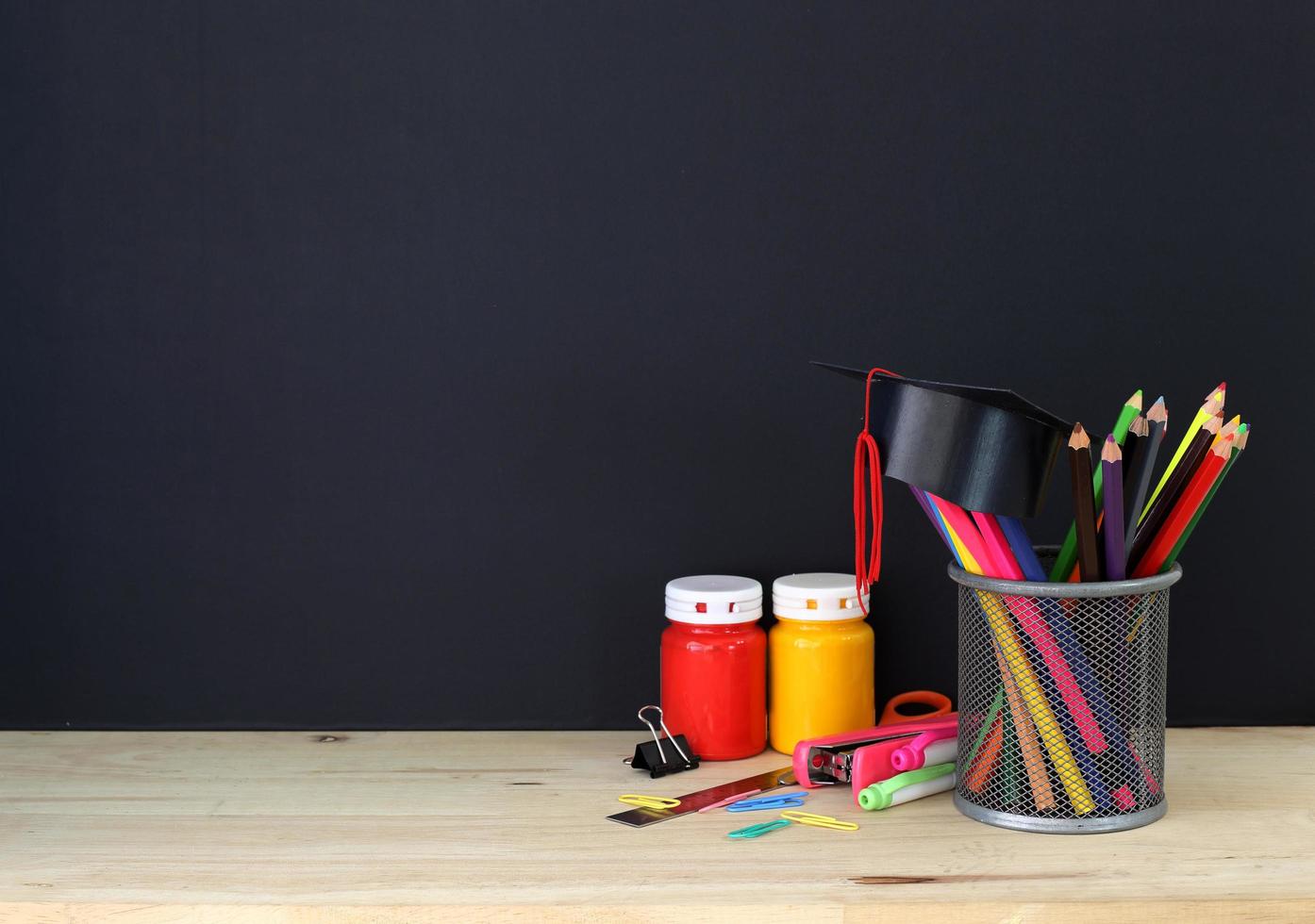 fournitures de papeterie colorées sur table en bois et chapeau de diplômé contre tableau noir photo