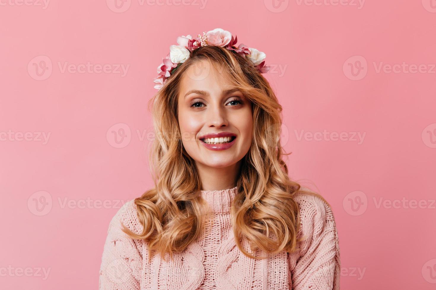 portrait en gros plan d'une fille blonde bouclée portant une couronne de fleurs et un pull tricoté sur fond rose photo