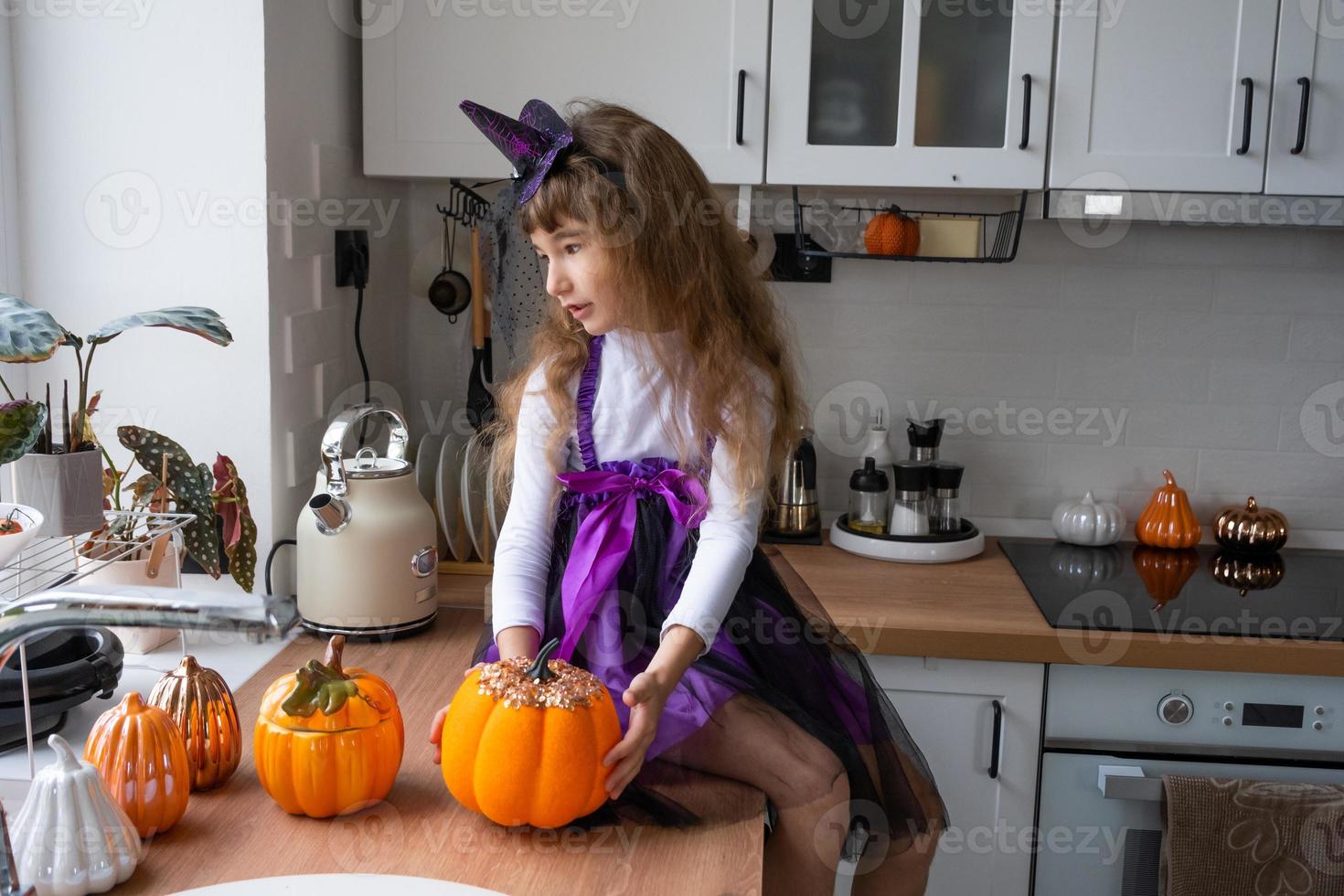 enfant décore la cuisine à la maison pour halloween. fille en costume de sorcière joue avec le décor pour les vacances - chauves-souris, lanterne jack, citrouilles. confort d'automne dans la maison, cuisine de style scandi, loft photo