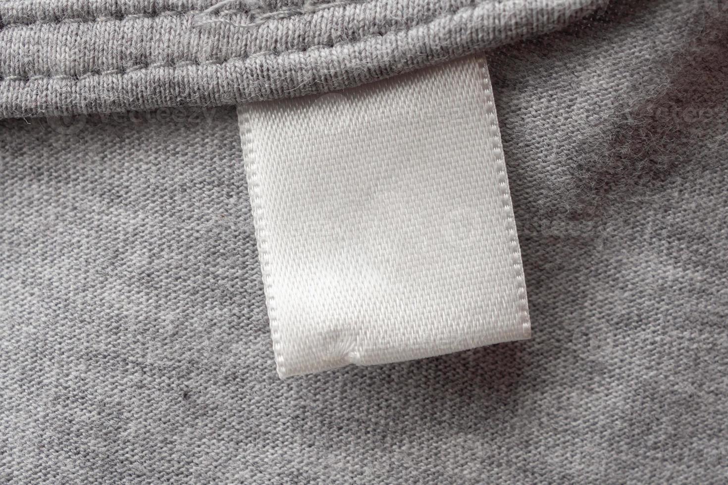 étiquette de vêtements de soin de lessive blanche vierge sur fond de texture de tissu gris photo