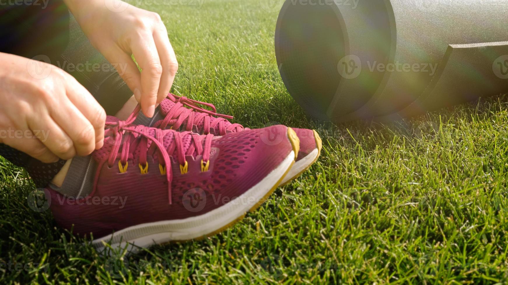 jeune femme attache les lacets sur la sneaker rose. femme se préparant pour le yoga asana ou l'entraînement de fitness sur la pelouse verte dans l'arrière-cour ou le parc. échauffez-vous avant de courir. mode de vie sain. photo