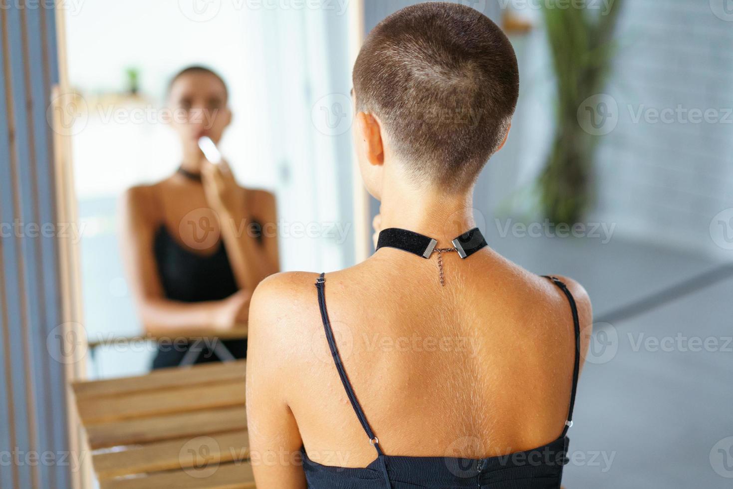 une fille aux cheveux courts peint ses lèvres, se regarde dans le miroir en vêtements noirs photo