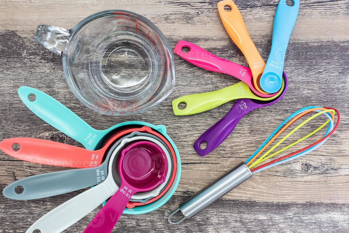 ensemble de tasses à mesurer, cuillères à mesurer, verre à mesurer et fouet en silicone utilisés dans la cuisine posés sur une table en bois en vue de dessus photo