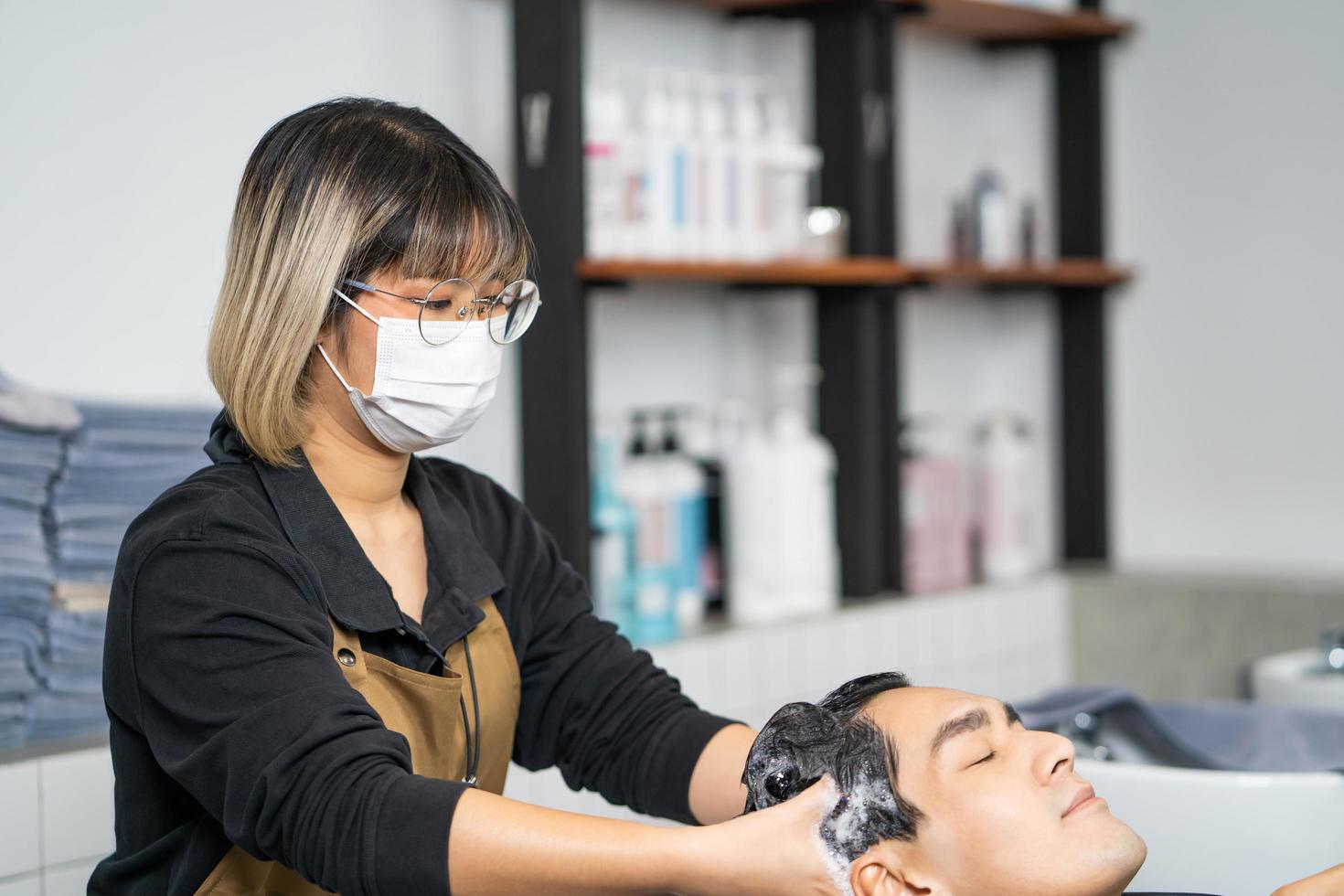 jeunes femmes asiatiques portant un masque chirurgical pendant que les cheveux se lavent avec du shampoing et un massage pour son client. studio de salon de coiffure avec des cheveux élégants, beauté et mode avec un nouveau concept normal après covid. photo