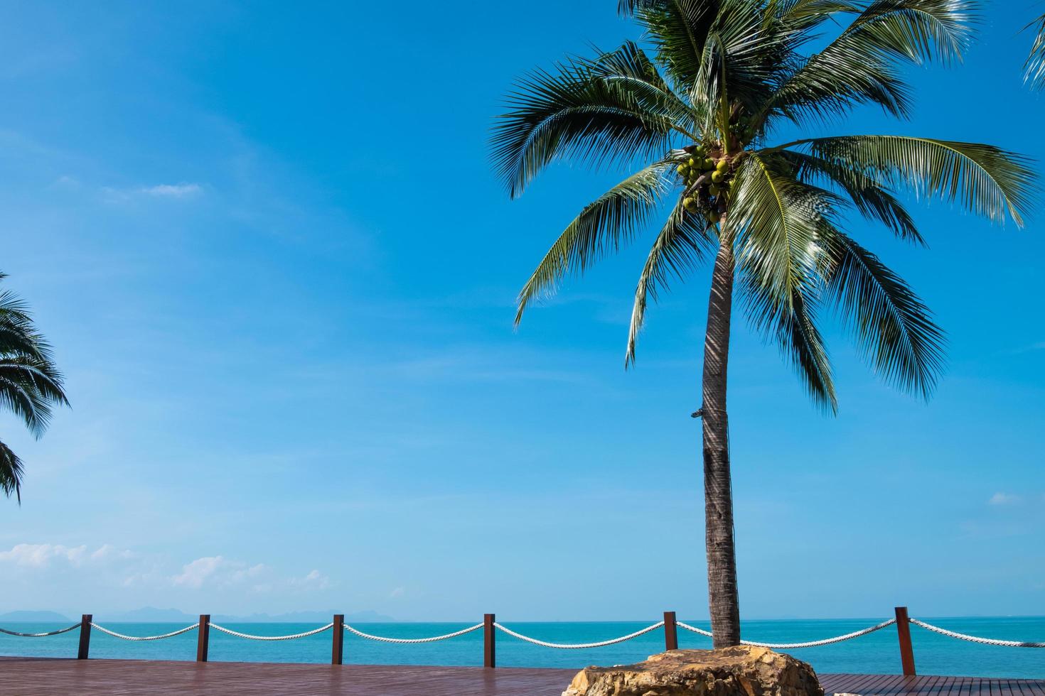 photo en plein air d'un magnifique paysage d'océan de plage avec une terrasse en bois à côté de la mer et du cocotier. avec ciel bleu clair, nuage et île. paysage tropical pour les vacances de vacances. avec espace libre