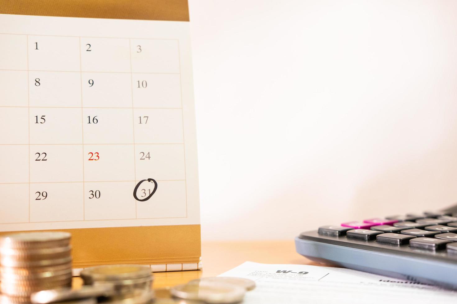 mise au point sélective au rappel du dernier jour du mois sur le calendrier. avec pile de pièces floues et calculatrice, formulaire de déclaration de revenus. date d'échéance des taxes ou des dépenses ou concept de jour de paiement avec espace de copie blanche. photo