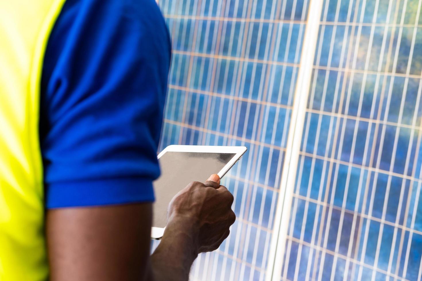 mise au point sélective sur tablette numérique. un ingénieur africain inspecte un panneau solaire électrique et enregistre des informations sur une tablette mobile. énergie alternative et concept industriel. prise de vue en extérieur. photo