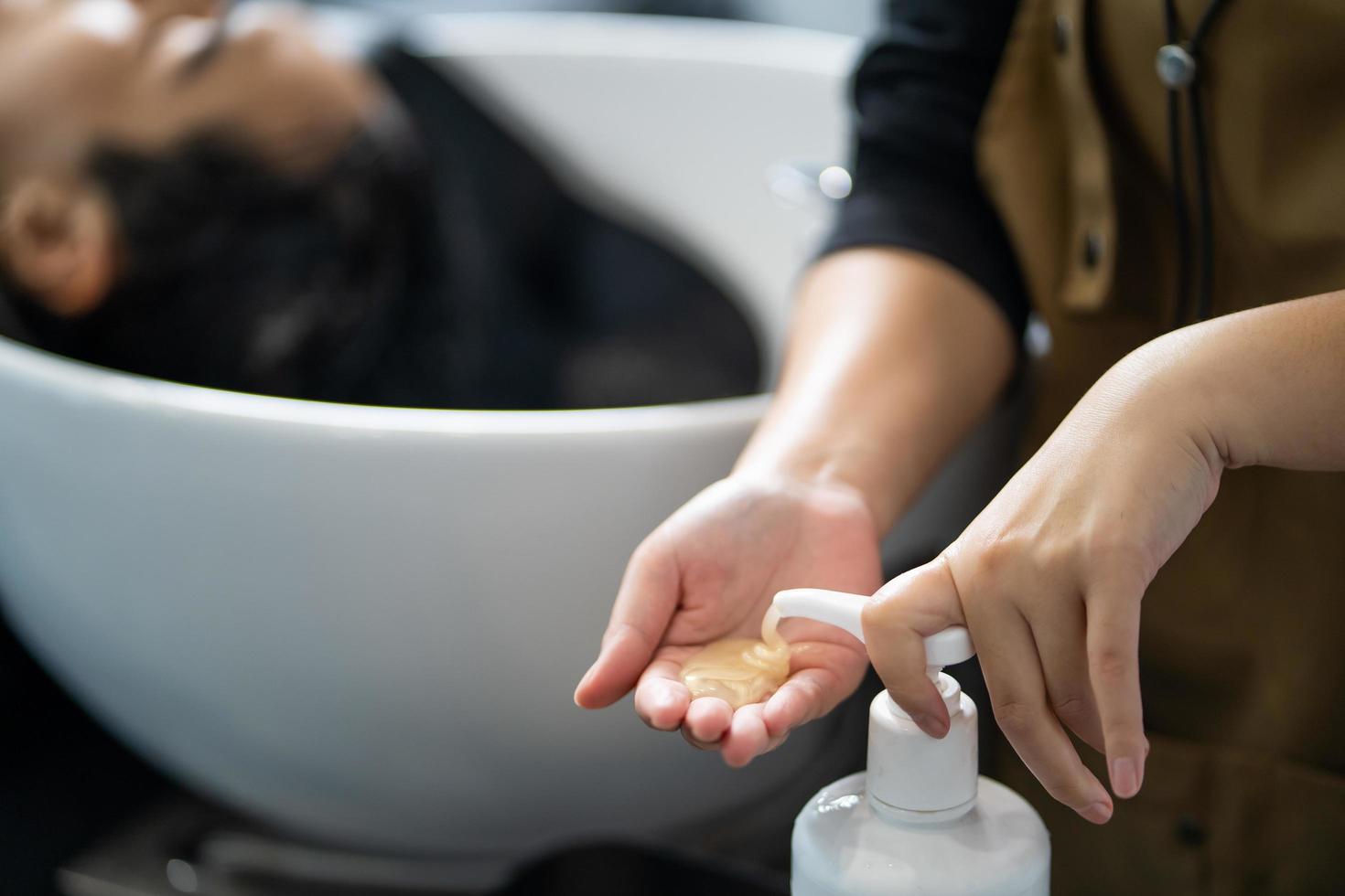 main de femmes coiffeur appuyez sur la bouteille de shampooing ou de revitalisant avant de l'utiliser pour laver le client à l'intérieur du studio de salon de coiffure. concept de produit et de service de beauté et de mode. photo