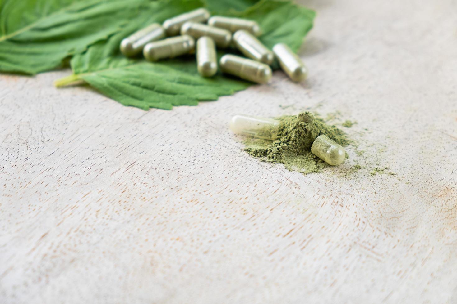 mise au point sélective sur la poudre à base de plantes. avec capsule d'herbe floue avec feuille à base de plantes sur fond en bois naturel avec espace de copie. médecine alternative qui peut guérir la maladie sans utiliser de drogue photo