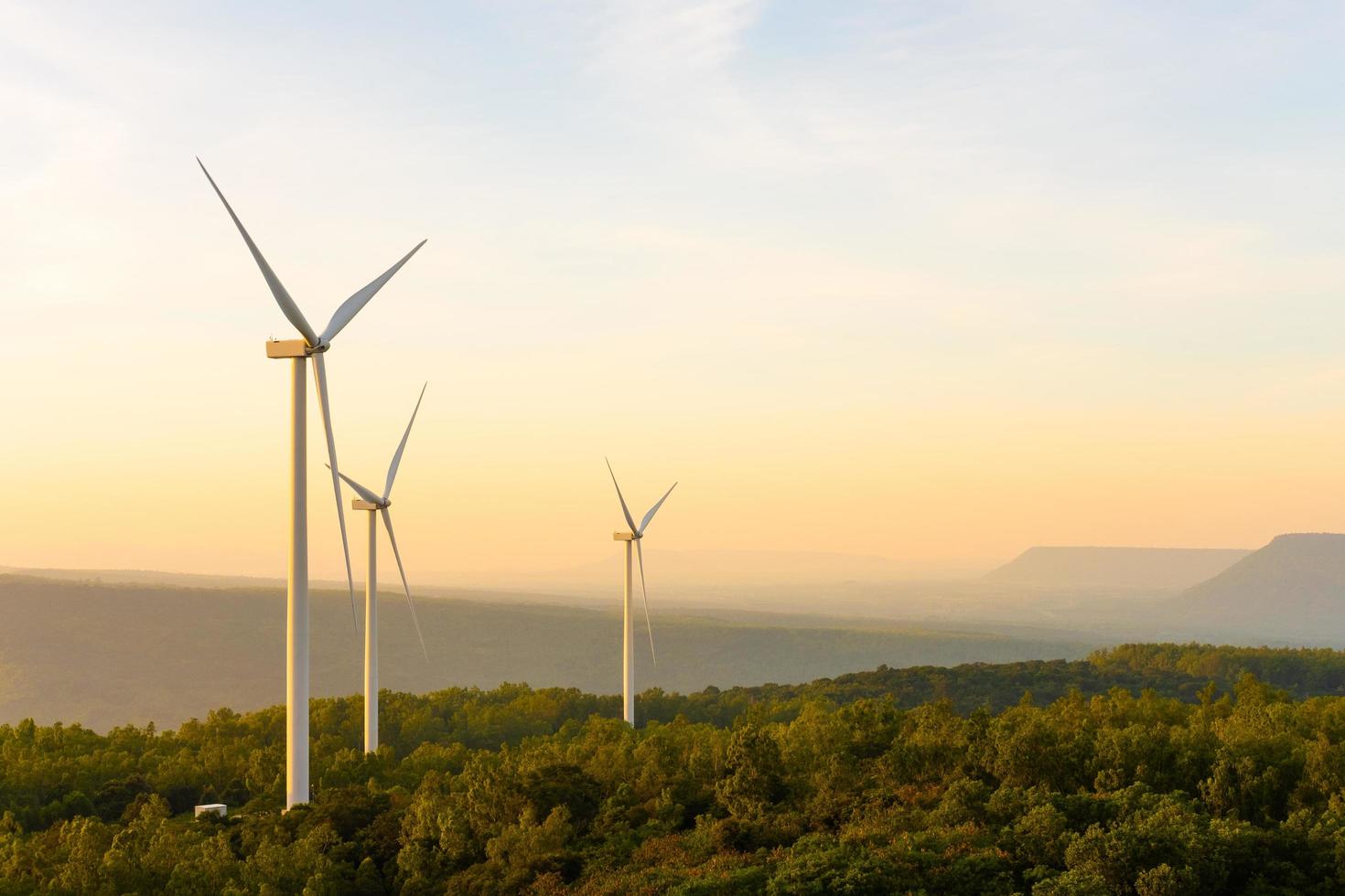 paysage coucher de soleil coup de ferme d'éoliennes sur le champ d'herbe verte avec ciel bleu clair et montagne à l'arrière-plan. énergie verte alternative qui génère de l'électricité à partir de l'énergie éolienne naturelle. photo