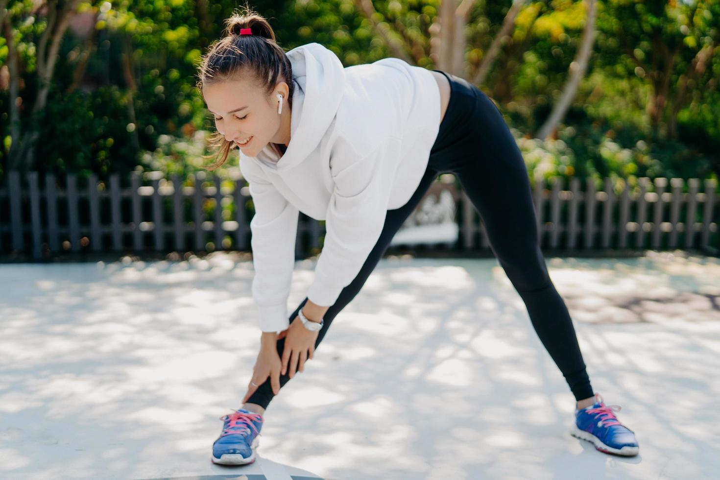 une jeune femme adulte motivée fait du sport atteint régulièrement la main aux pieds se penche vers le bas a les pieds écartés de la largeur des épaules porte des vêtements de sport aime s'entraîner activités sportives de plein air pour perdre du poids photo