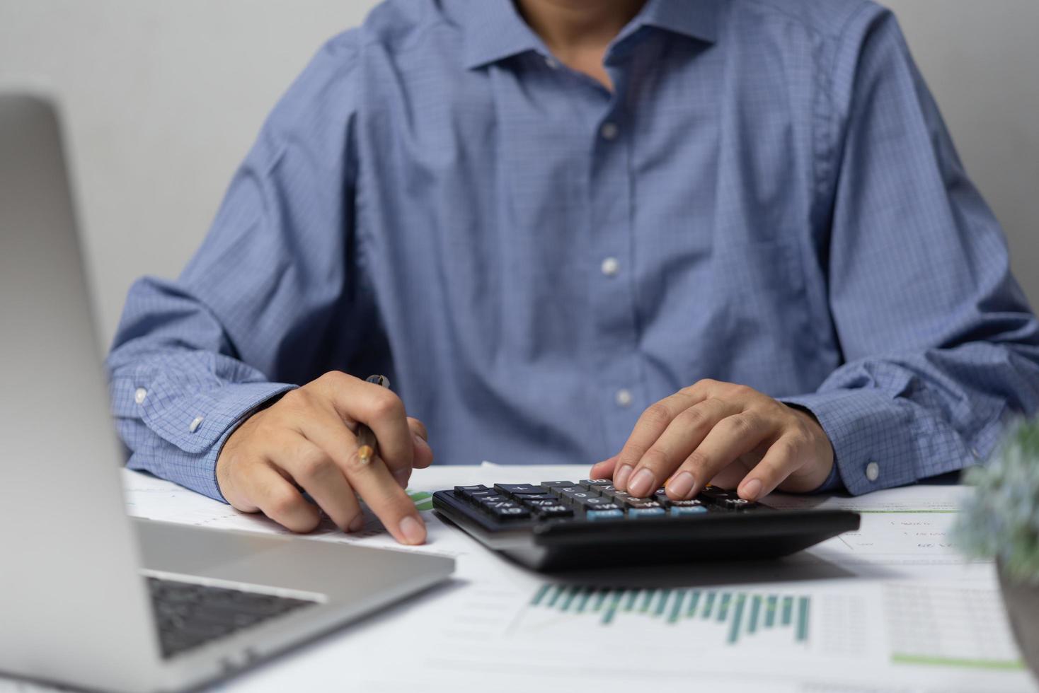 main d'homme d'affaires à l'aide d'une calculatrice tenant un stylo et faisant de la finance et de la comptabilité fiscale sur le bureau au bureau à domicile. photo