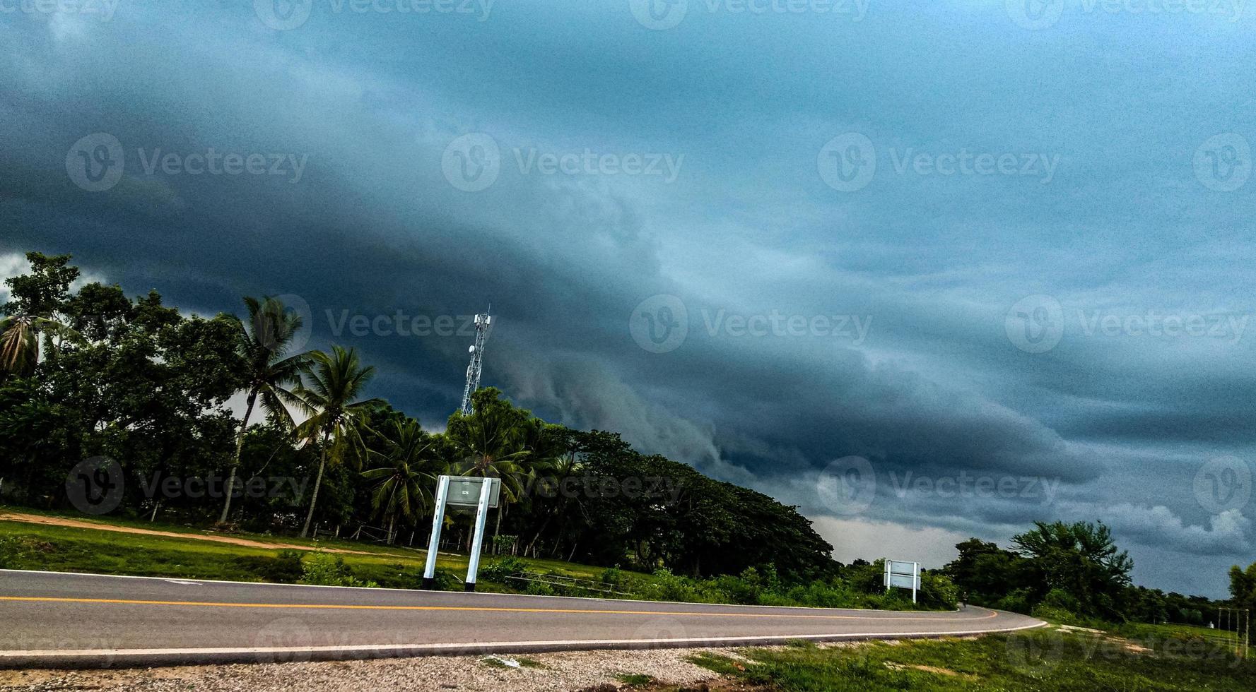 des nuages d'orage noirs se forment sur une route noire entourée de forêts vertes. prévisions météorologiques de la saison de la mousson. photo