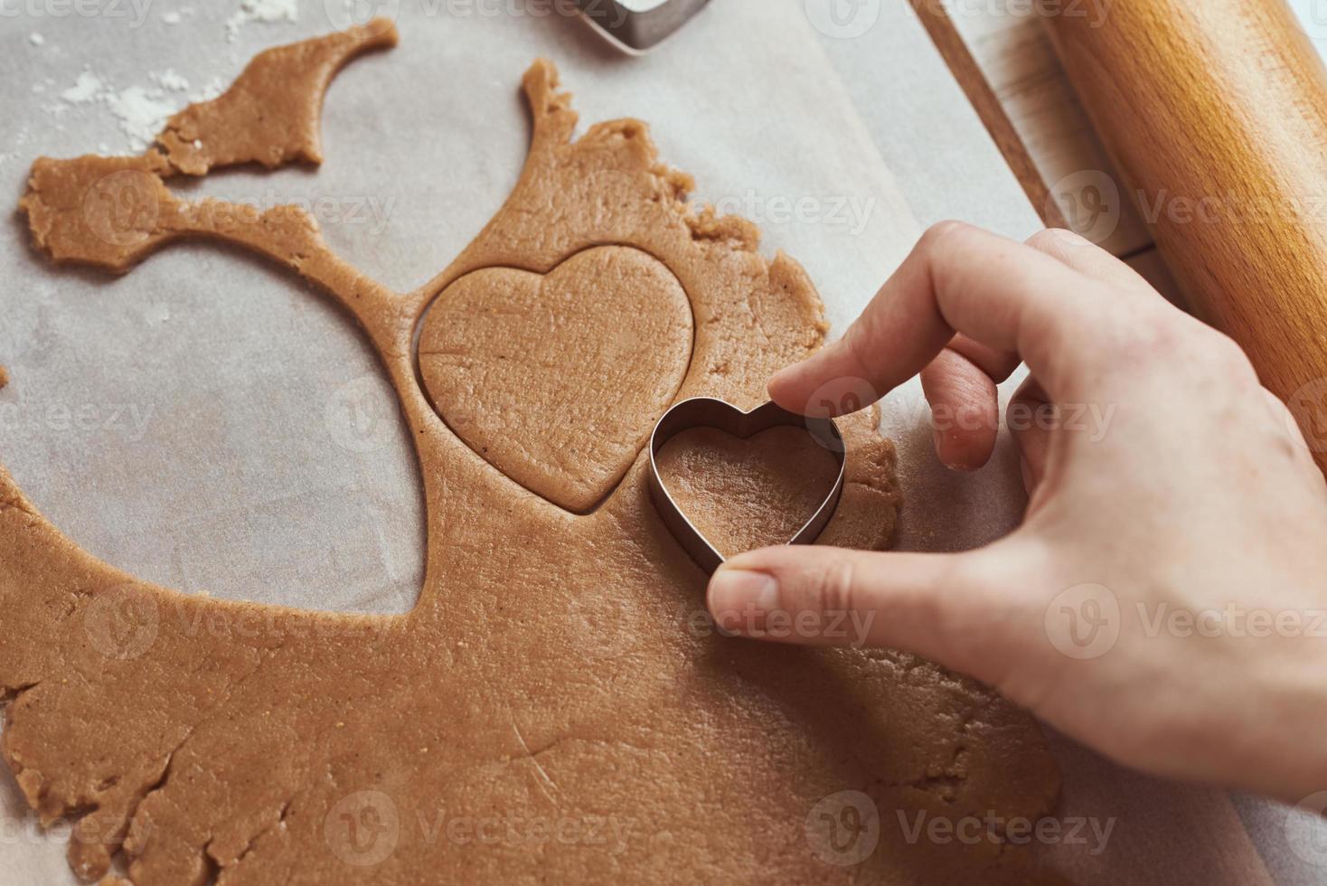 faire des biscuits au pain d'épice en forme de coeur pour la saint valentin. main de femme utilise un emporte-pièce. concept de nourriture de vacances photo