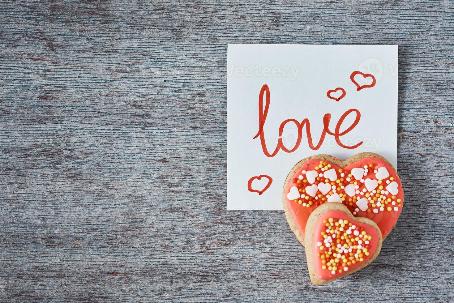 biscuits en forme de coeur décorés et vitrés et note papier avec inscription love sur fond gris, vue de dessus. concept de la saint valentin photo