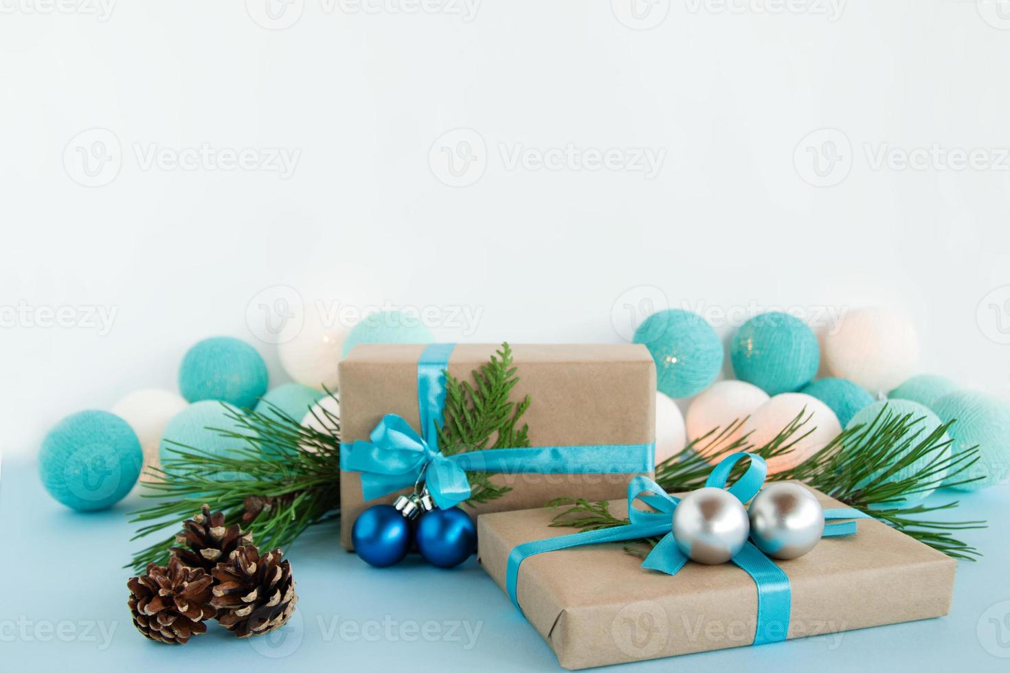 deux coffrets cadeaux de noël enveloppés de papier kraft, de rubans bleus et blancs, décorés de branches de sapin, de boules de noël et de pommes de pin sur fond bleu et blanc avec des lumières de noël. photo