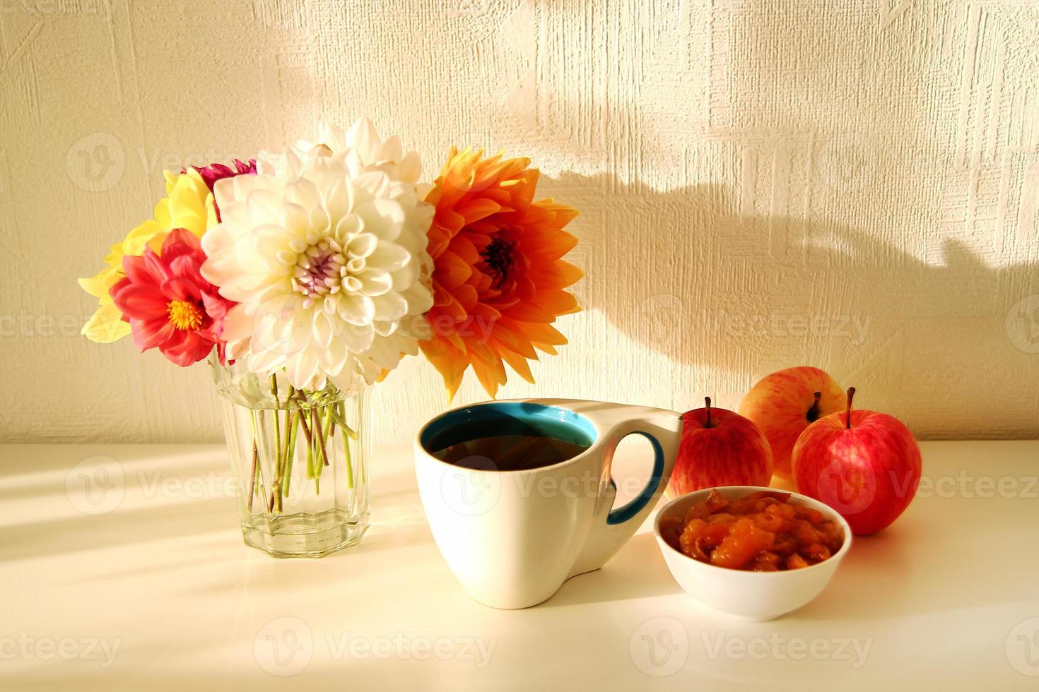 nature morte avec vase en verre avec fleurs colorées de pivoines, tasse de thé, confiture de pomme et pommes sur le tableau blanc sous une lumière ensoleillée. photo