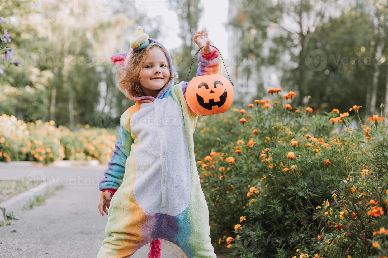 jolie petite fille en costume de licorne arc-en-ciel pour halloween va chercher des bonbons dans un panier de citrouille dans un quartier résidentiel. l'enfant marche à l'extérieur. La charité s'il-vous-plaît. mode de vie. kigurumi photo